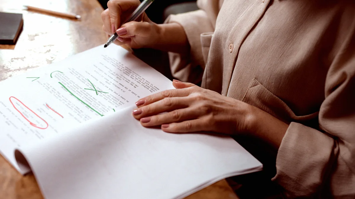 Mains d'une relectrice annotant au feutre vert un document imprimé déjà marqué de corrections rouges et vertes