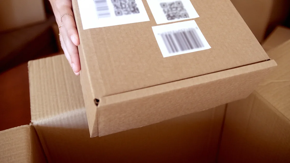 Mains déposant un colis en carton étiqueté de codes-barres dans un carton d'expédition ouvert