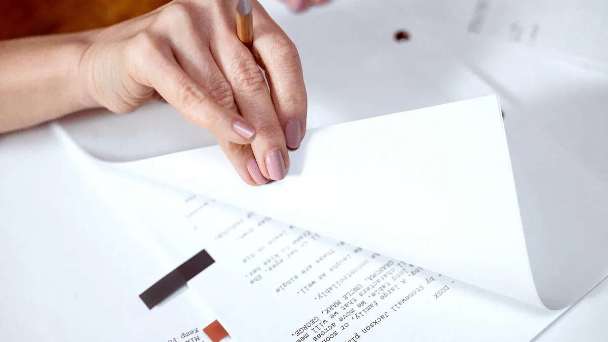 Main feuilletant les pages imprimées d'un document de travail posé sur un bureau