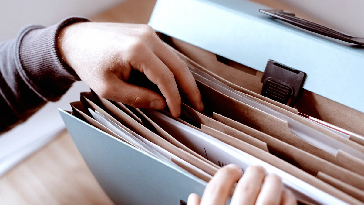 Mains feuilletant des dossiers suspendus rangés dans une boîte d'archives