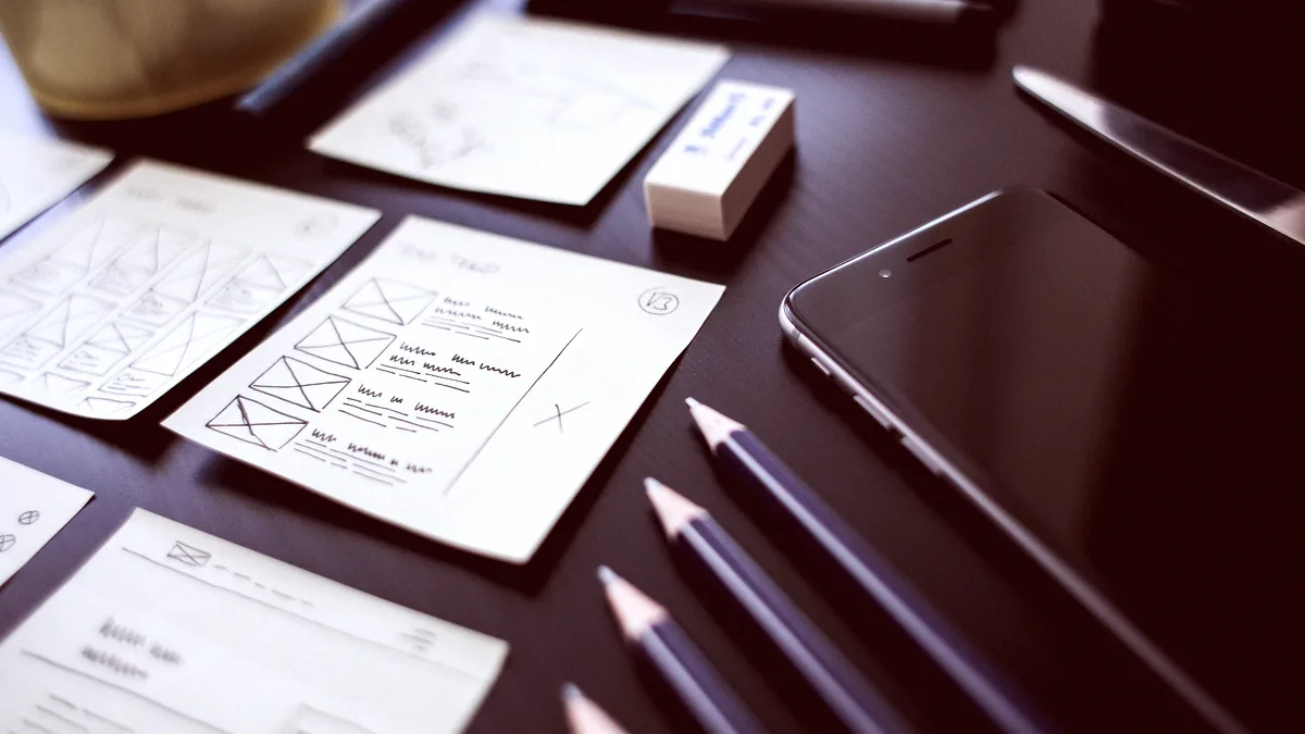Croquis de wireframes au feutre étalés sur un bureau sombre, crayons et smartphone à côté